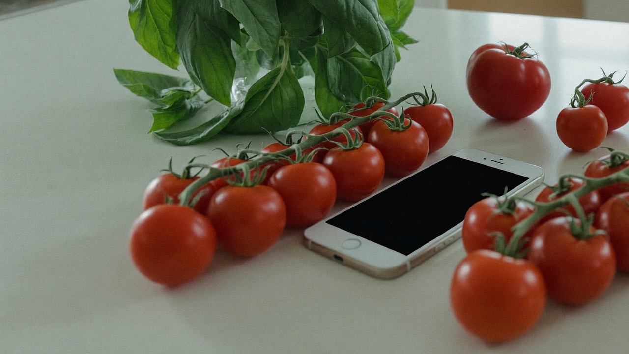A smartphone lying on a kitchen counter beside vine tomatoes and fresh basil